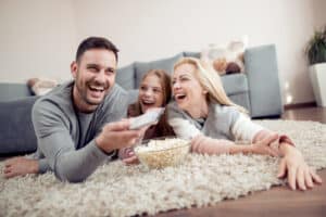 Father,mother and daughter lying on floor,watching TV and eating popcorn.