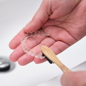 Patient using toothbrush to clean aligners in sink