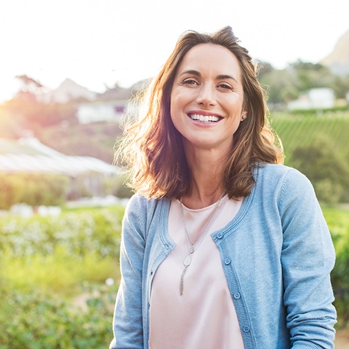 a smiling woman wearing a blue cardigan standing outside