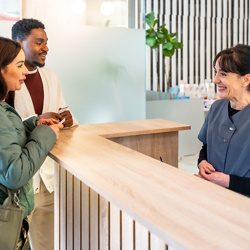 a couple speaking with a front desk staff member at a dental office