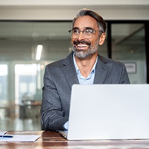 Man with glasses smiling while working on computer in office