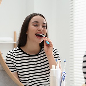 Woman smiling while brushing her teeth in bathroom