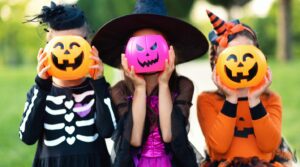 Kids dressed in Halloween costumes holding jack-o-lanterns over their faces.